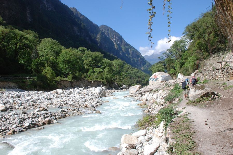 Trekkers walking beside a river in a lush mountain valley.